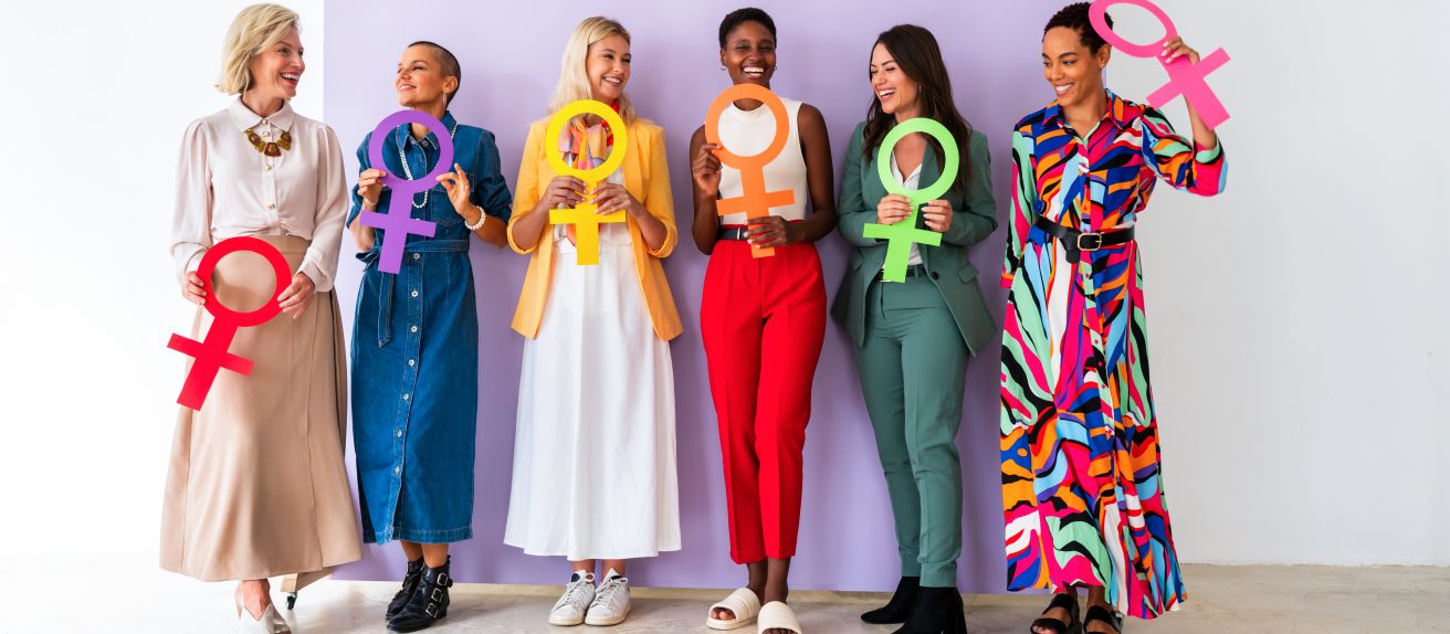 Groupe de femmes souriantes tenant des symboles féminins colorés devant un fond violet.