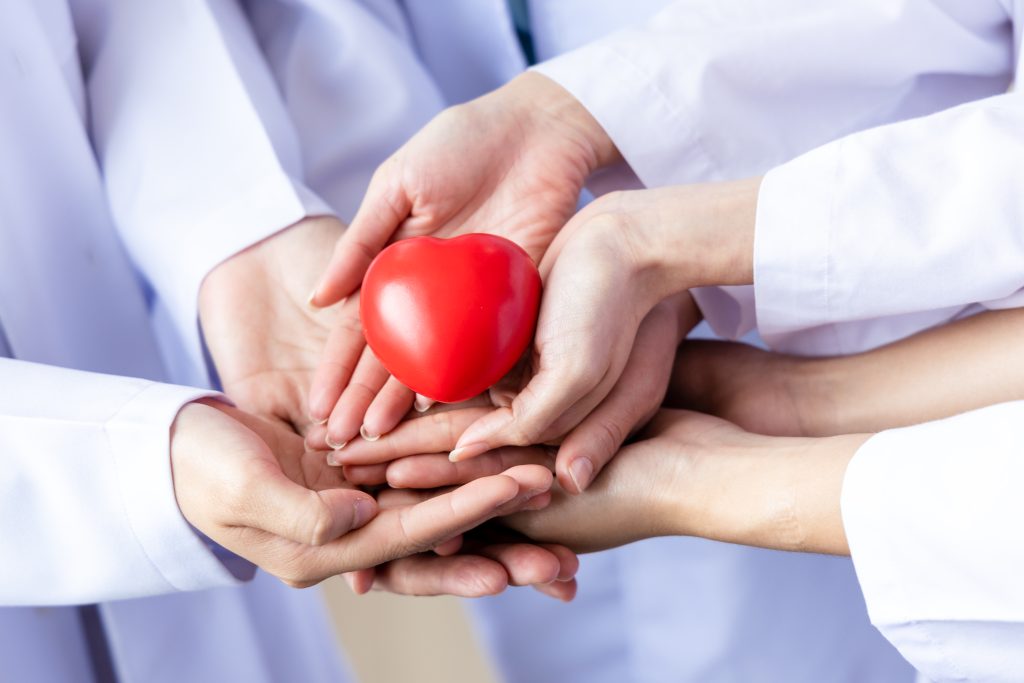 Plusieurs mains de professionnels de santé tiennent ensemble un cœur rouge symbolique.