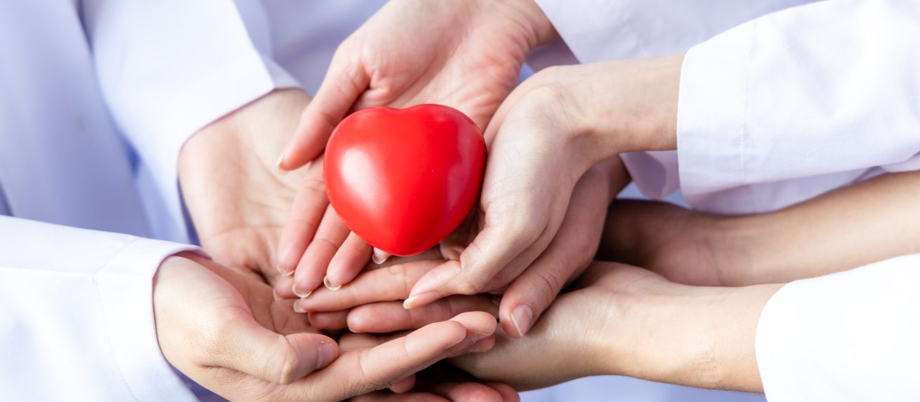 Plusieurs mains de professionnels de santé tiennent ensemble un cœur rouge symbolique.