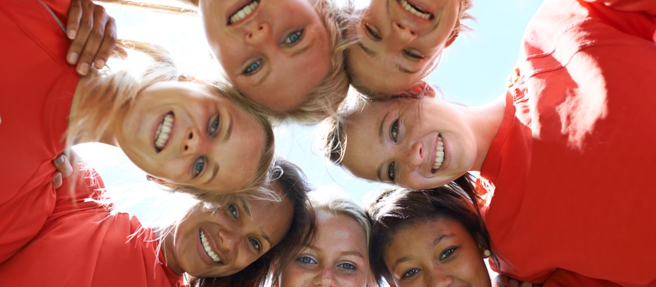 Un groupe de jeunes femmes souriantes regarde vers le bas en formant un cercle.