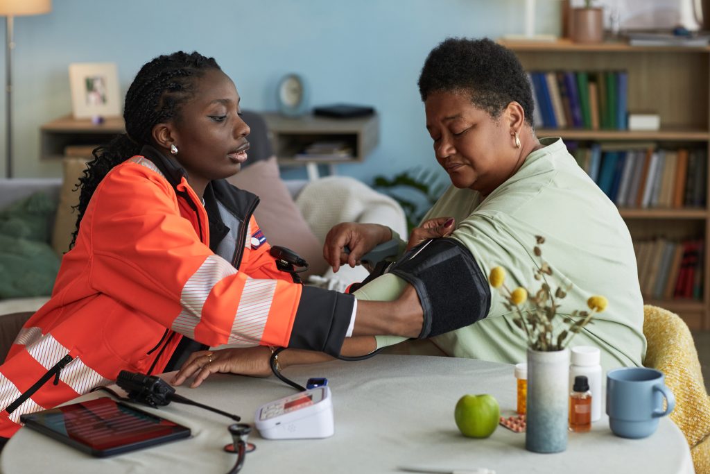 Professionnelle de santé prenant la tension d’une femme à domicile.