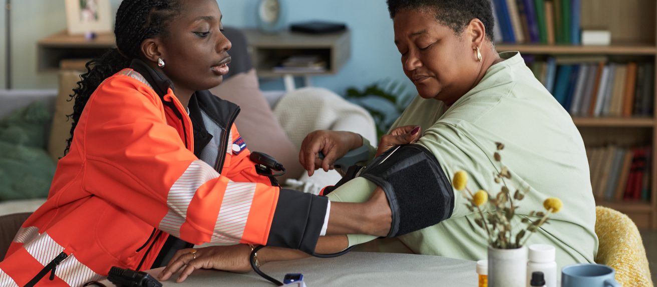Professionnelle de santé prenant la tension d’une femme à domicile.