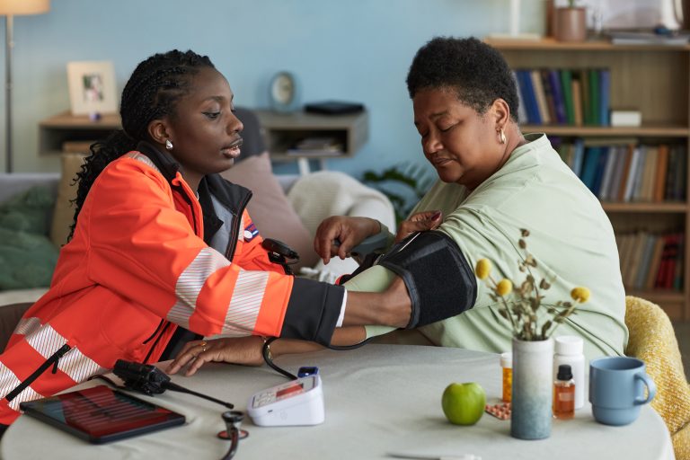 Professionnelle de santé prenant la tension d’une femme à domicile.
