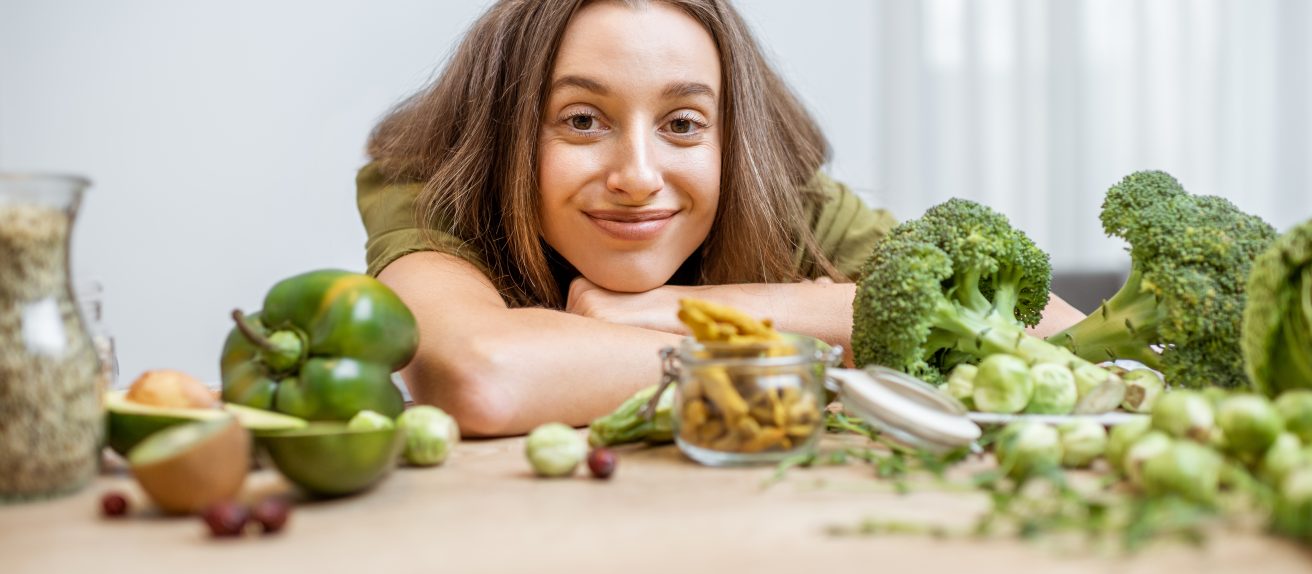 Une femme souriante entourée de légumes verts symbolisant une alimentation bénéfique pour la santé cardiovasculaire
